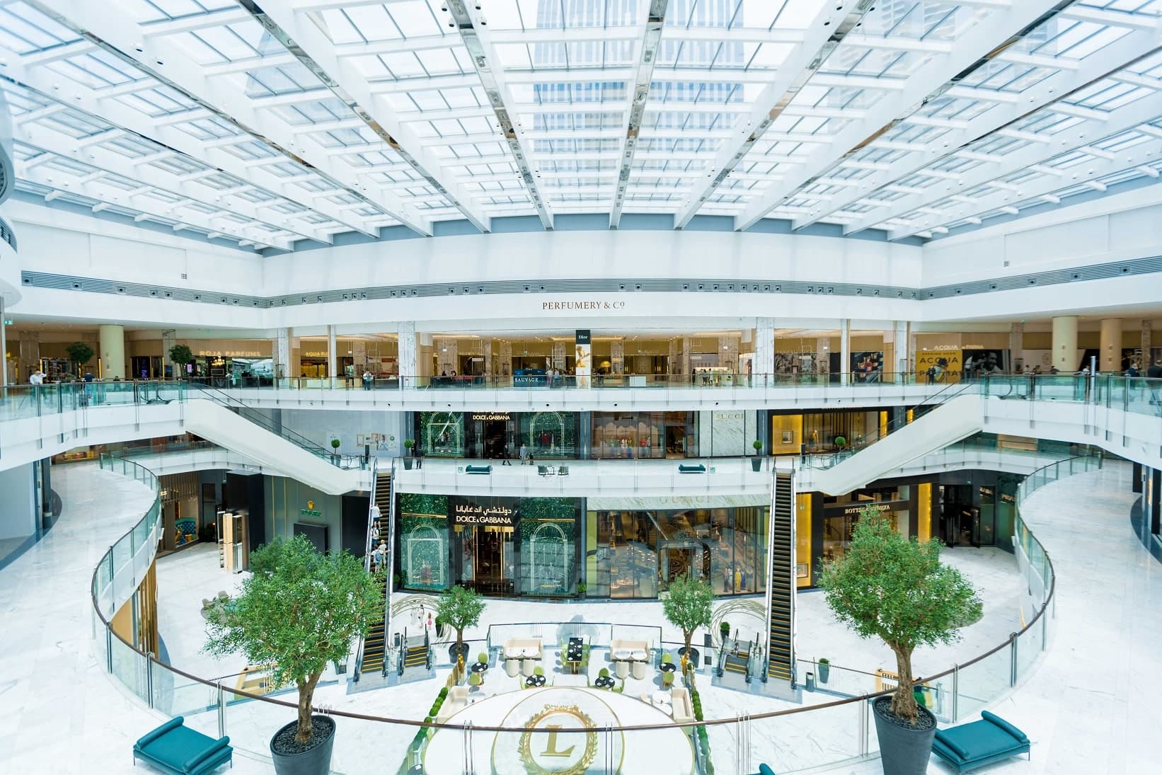 Bright, multi-level luxury shopping mall atrium with skylights, escalators, and designer boutiques